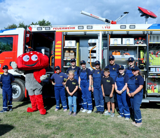 Lotties Welt: 25.000 € für Jugendfeuerwehren Ein Fliegenpilz Maskottchen steht zusammen mit Kinder vor einem Feuerwehrwagen.