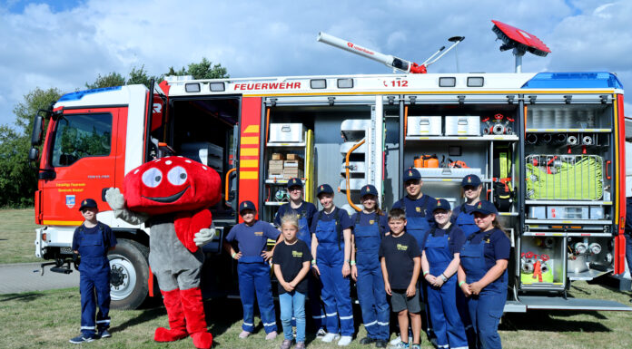 Lotties Welt: 25.000 € für Jugendfeuerwehren Ein Fliegenpilz Maskottchen steht zusammen mit Kinder vor einem Feuerwehrwagen.