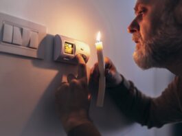 3 wichtige Fragen zur bevorstehenden Gaskrise Gas und Strom sparen: Mann in völliger Dunkelheit, der eine Kerze hält, um Thermostat während eines Stromausfalls zu untersuchen.