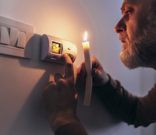 3 wichtige Fragen zur bevorstehenden Gaskrise Gas und Strom sparen: Mann in völliger Dunkelheit, der eine Kerze hält, um Thermostat während eines Stromausfalls zu untersuchen.