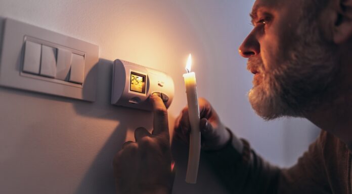 3 wichtige Fragen zur bevorstehenden Gaskrise  Gas und Strom sparen: Mann in völliger Dunkelheit, der eine Kerze hält, um Thermostat während eines Stromausfalls zu untersuchen.
