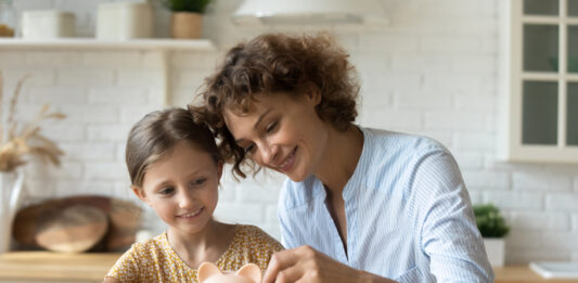 Weltspartag: Die Ergebnisse des Vermögensbarometers Weltspartag: Eine Mutter und ihre Tochter stecken Geld in ein Sparschwein.