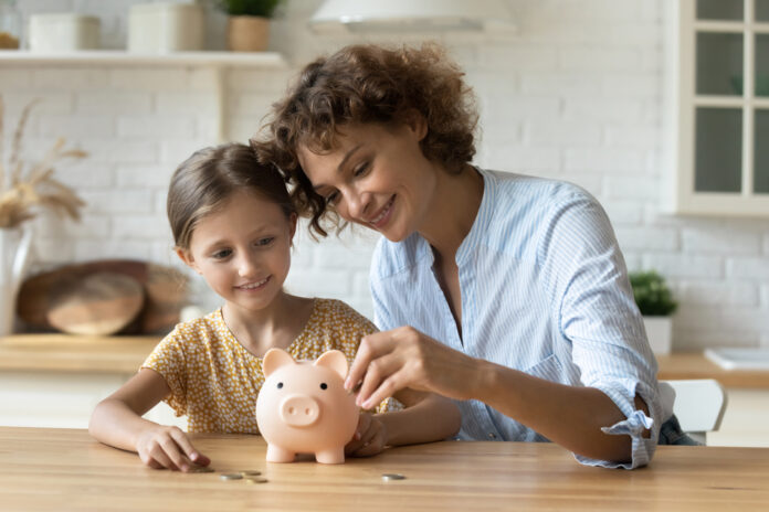 Weltspartag: Eine Mutter und ihre Tochter stecken Geld in ein Sparschwein.