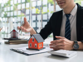 Warum Bausparverträge ein Comeback erleben Ein Bankkaufmann sitzt am Schreibtisch mit einem Vertrag, auf dem ein kleines rotes Haus steht.