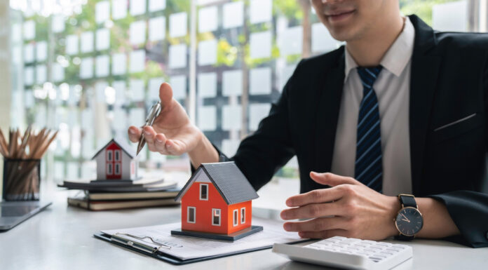 Warum Bausparverträge ein Comeback erleben Ein Bankkaufmann sitzt am Schreibtisch mit einem Vertrag, auf dem ein kleines rotes Haus steht.