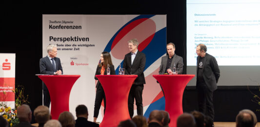 Gestörte Lieferketten: Fachkonferenz in der Förde Sparkasse Eine Frau und vier Männer diskutieren auf einer Bühne vor Publikum