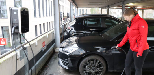 Echt nachhaltig: Förde Sparkasse unterstützt Verkehrswende Eine Mitarbeiterin der Förde Sparkasse lädt ihr E-Auto an einer Ladesäule auf.