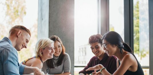 Sparen mit Aktien bei jungen Menschen immer beliebter Junge Studentinnen tauschen sich am Tisch aus.