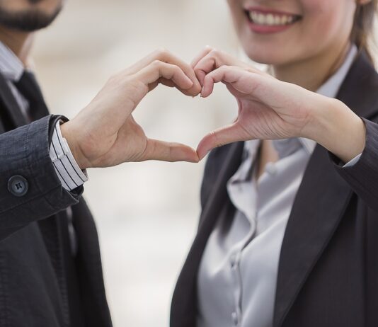 Liebe am Arbeitsplatz Ein Mann und eine Frau formen mit ihren Händen ein Herz