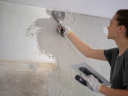 Muskelhypothek – beim Hausbau anpacken und Geld sparen Junge Frau, die Hausreparaturen durch Auftragen eines Pflasters mit einem Tuch durchführt.