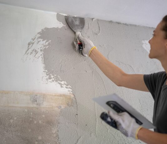 Muskelhypothek – beim Hausbau anpacken und Geld sparen Junge Frau, die Hausreparaturen durch Auftragen eines Pflasters mit einem Tuch durchführt.