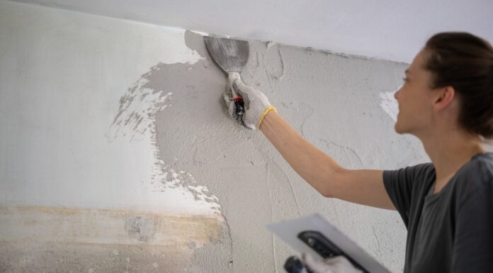 Muskelhypothek – beim Hausbau anpacken und Geld sparen Junge Frau, die Hausreparaturen durch Auftragen eines Pflasters mit einem Tuch durchführt.