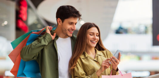 Bonusprogramme in Zeiten von Inflation: Das Instrument zur Kundenbindung und Neukundengewinnung im Einzelhandel Paar beim Shoppen mit Smartphone in der Hand. Bonusprogramm zur Kundenbindung.