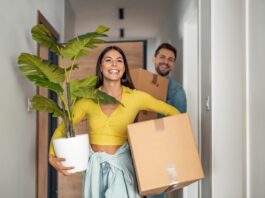 Bezahlbarer Wohnraum – eine Übersicht Junges Ehepaare zieht in neues Zuhause um mit Kartons und Pflanze.