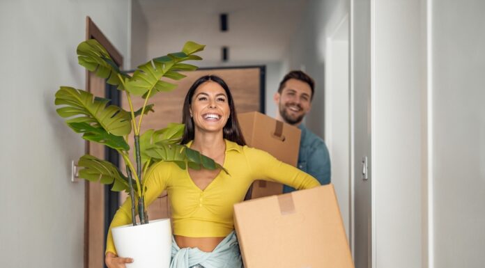 Bezahlbarer Wohnraum – eine Übersicht Junges Ehepaare zieht in neues Zuhause um mit Kartons und Pflanze.