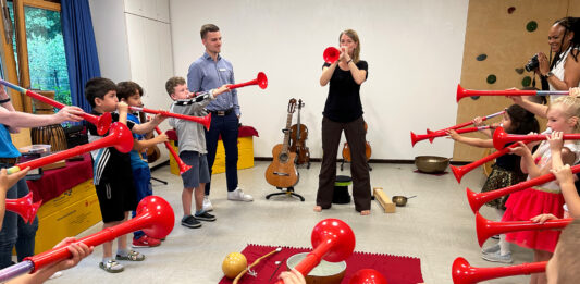 musiculum MOBIL: 60 kostenlose Kita-Einsätze durch die Sparkassen in S-H Eine Frau und viele Kinder blasen in rote Tröten.