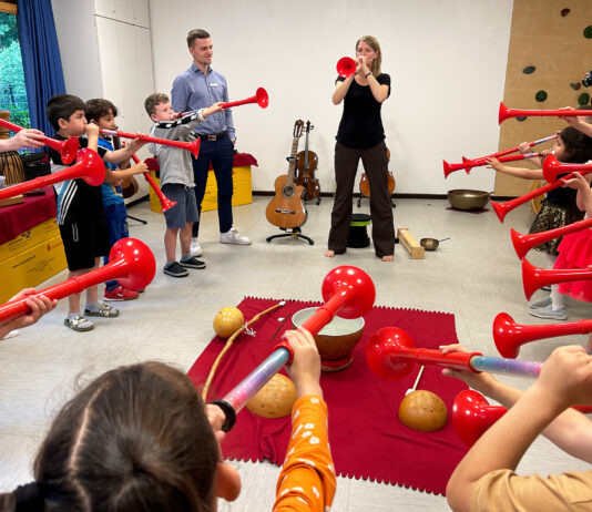musiculum MOBIL: 60 kostenlose Kita-Einsätze durch die Sparkassen in S-H Eine Frau und viele Kinder blasen in rote Tröten.