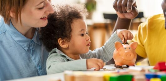 Kindergrundsicherung: Was sich nun ändert Ein Kind steckt eine Münze in ein Sparschwein