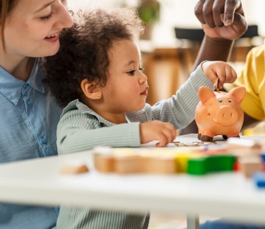 Kindergrundsicherung: Was sich nun ändert Ein Kind steckt eine Münze in ein Sparschwein