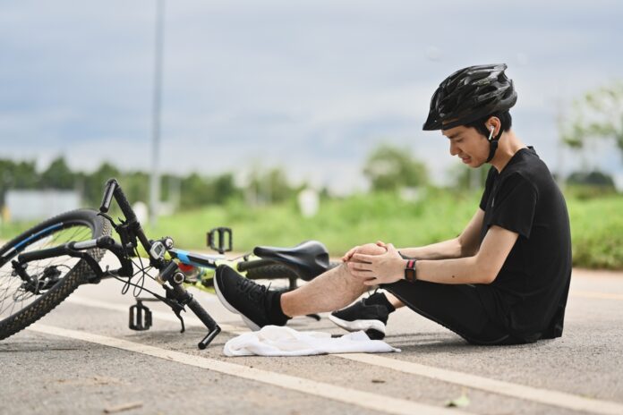 Junger Radfahrer, der einen Unfall hatte, vom Fahrrad herunterfiel und sein Knie verletzte
