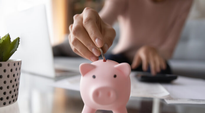 Notgroschen: Wie viel Geld sollte ich beiseitelegen? Nahaufnahme von junger Frau, die Münze im Sparschwein einsetzt.