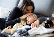 Kinderkrankengeld: Das sind Ihre Ansprüche Kleiner blonder Junge schläft im Arm seiner Mutter auf dem Sofa, daneben Medikamente