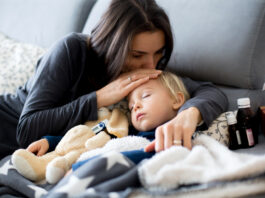 Kinderkrankengeld: Das sind Ihre Ansprüche Kleiner blonder Junge schläft im Arm seiner Mutter auf dem Sofa, daneben Medikamente