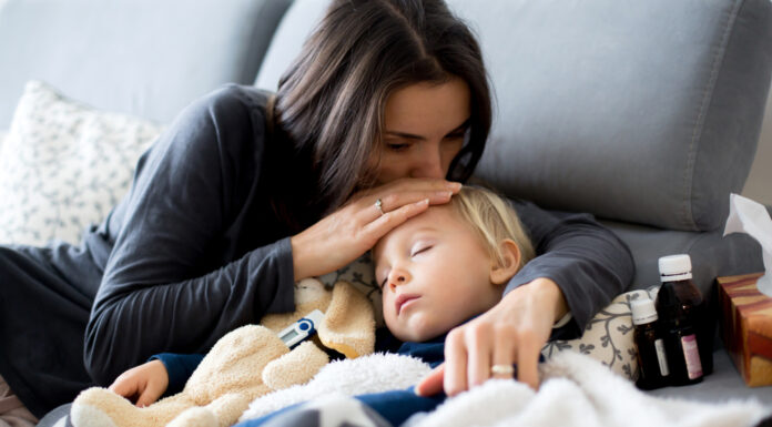 Kinderkrankengeld: Das sind Ihre Ansprüche Kleiner blonder Junge schläft im Arm seiner Mutter auf dem Sofa, daneben Medikamente