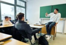 Tatort soziale Netzwerke: Verschwörungsmythen und Fake News im Internet Ein Mann sitzt vor einer Schulklasse auf einem Tisch vor einer Tafel.