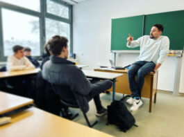 Tatort soziale Netzwerke: Verschwörungsmythen und Fake News im Internet Ein Mann sitzt vor einer Schulklasse auf einem Tisch vor einer Tafel.