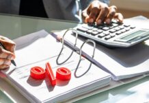 Mit Wertpapieren von Zinsen profitieren – so geht’s jetzt am besten! Mann rechnet mit Taschenrechner, Prozentzeichen liegt auf der Akte