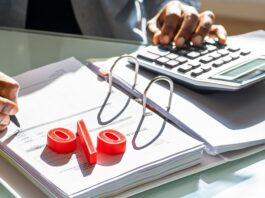 Mit Wertpapieren von Zinsen profitieren – so geht’s jetzt am besten! Mann rechnet mit Taschenrechner, Prozentzeichen liegt auf der Akte