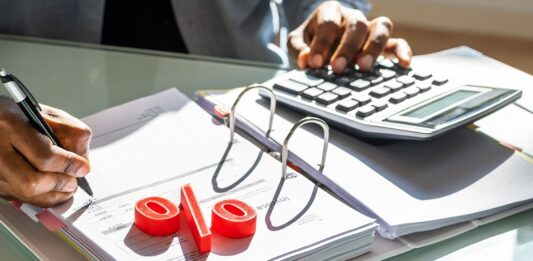 Mit Wertpapieren von Zinsen profitieren – so geht’s jetzt am besten! Mann rechnet mit Taschenrechner, Prozentzeichen liegt auf der Akte