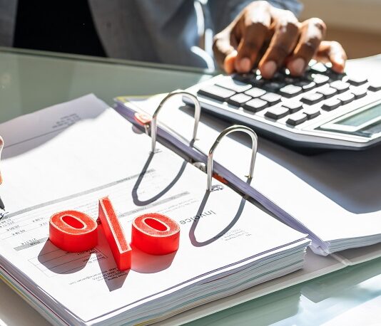 Mit Wertpapieren von Zinsen profitieren – so geht’s jetzt am besten! Mann rechnet mit Taschenrechner, Prozentzeichen liegt auf der Akte