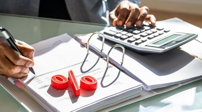 Mit Wertpapieren von Zinsen profitieren – so geht’s jetzt am besten! Mann rechnet mit Taschenrechner, Prozentzeichen liegt auf der Akte