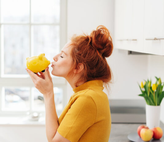 Die 5 besten Spar-Challenges – Kreative Spartipps Rothaarige Frau küsst ein gelbes Sparschwein