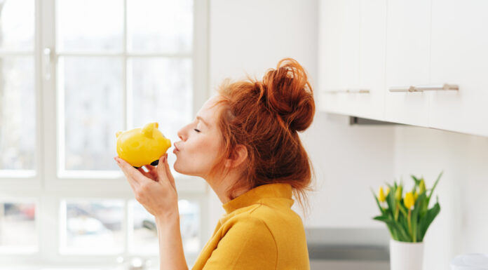 Die 5 besten Spar-Challenges – Kreative Spartipps Rothaarige Frau küsst ein gelbes Sparschwein