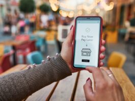 „Buy now, pay later” – Flexibilität oder Schuldenfalle? Frauenhände halten Smartphone, auf dem Buy New Pay Later steht
