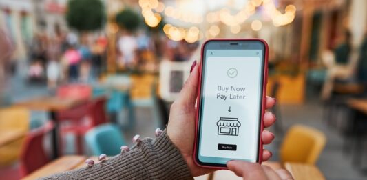 „Buy now, pay later” – Flexibilität oder Schuldenfalle? Frauenhände halten Smartphone, auf dem Buy New Pay Later steht