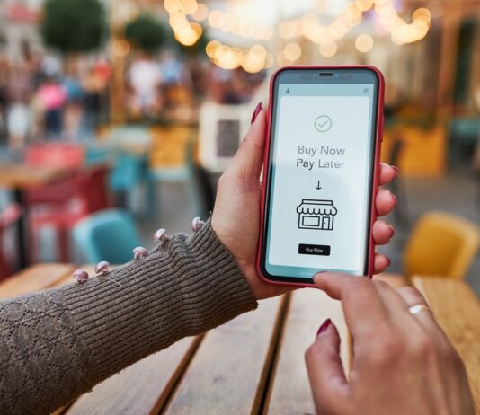 „Buy now, pay later” – Flexibilität oder Schuldenfalle? Frauenhände halten Smartphone, auf dem Buy New Pay Later steht