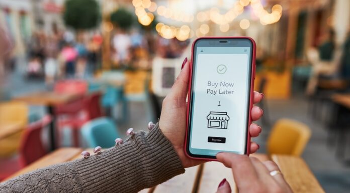 „Buy now, pay later” – Flexibilität oder Schuldenfalle? Frauenhände halten Smartphone, auf dem Buy New Pay Later steht