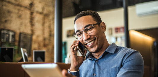 Live-Chat, Social Media, Avatare: Die Vielfalt der digitalen Kundenkommunikation Ein junger POC telefoniert und hat ein Tablet in der Hand.