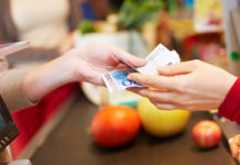 Bargeldservice in Supermärkten & Co. Eine Hand reicht an einer Supermarkt Kasse Euroscheine an eine andere Hand weiter.