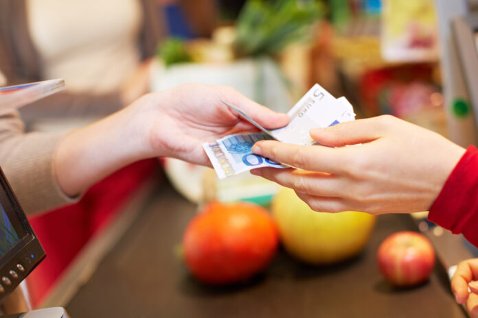 Eine Hand reicht an einer Supermarkt Kasse Euroscheine an eine andere Hand weiter.