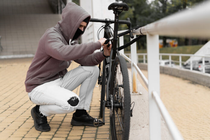 Ein Dieb in einer Balaclava und mit einer Kapuze bricht das Schloss an einem Fahrrad auf der Straße auf.