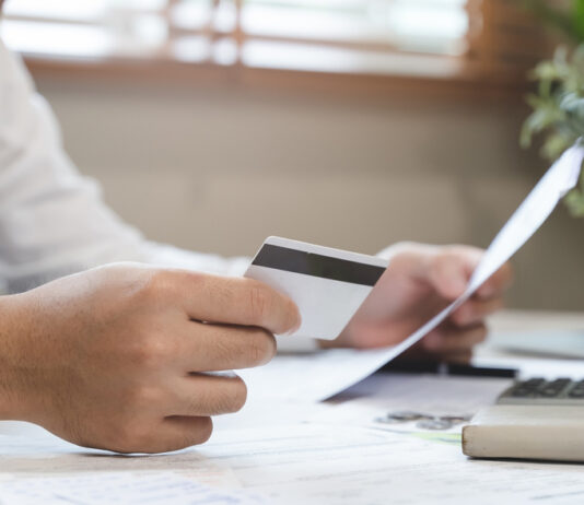 Auslagen und Spesen – 8 Tipps für mehr Effizienz in Unternehmen Ein Mann sitzt am Schreibtisch und hält eine Kreditkarte und Rechnungen in der Hand.