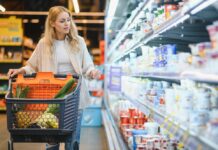 Inflationsrate: Was wurde wie viel teurer seit 2019? Junge blonde Frau, die Produkte im Kühlregal eines Lebensmittelgeschäftes anschaut.