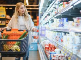 Inflationsrate: Was wurde wie viel teurer seit 2019? Junge blonde Frau, die Produkte im Kühlregal eines Lebensmittelgeschäftes anschaut.