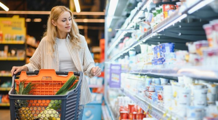Inflationsrate: Was wurde wie viel teurer seit 2019? Junge blonde Frau, die Produkte im Kühlregal eines Lebensmittelgeschäftes anschaut.