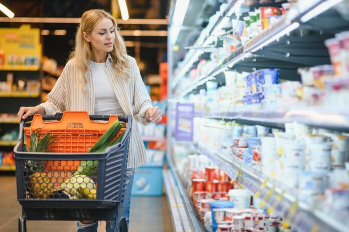 Junge blonde Frau, die Produkte im Kühlregal eines Lebensmittelgeschäftes anschaut.